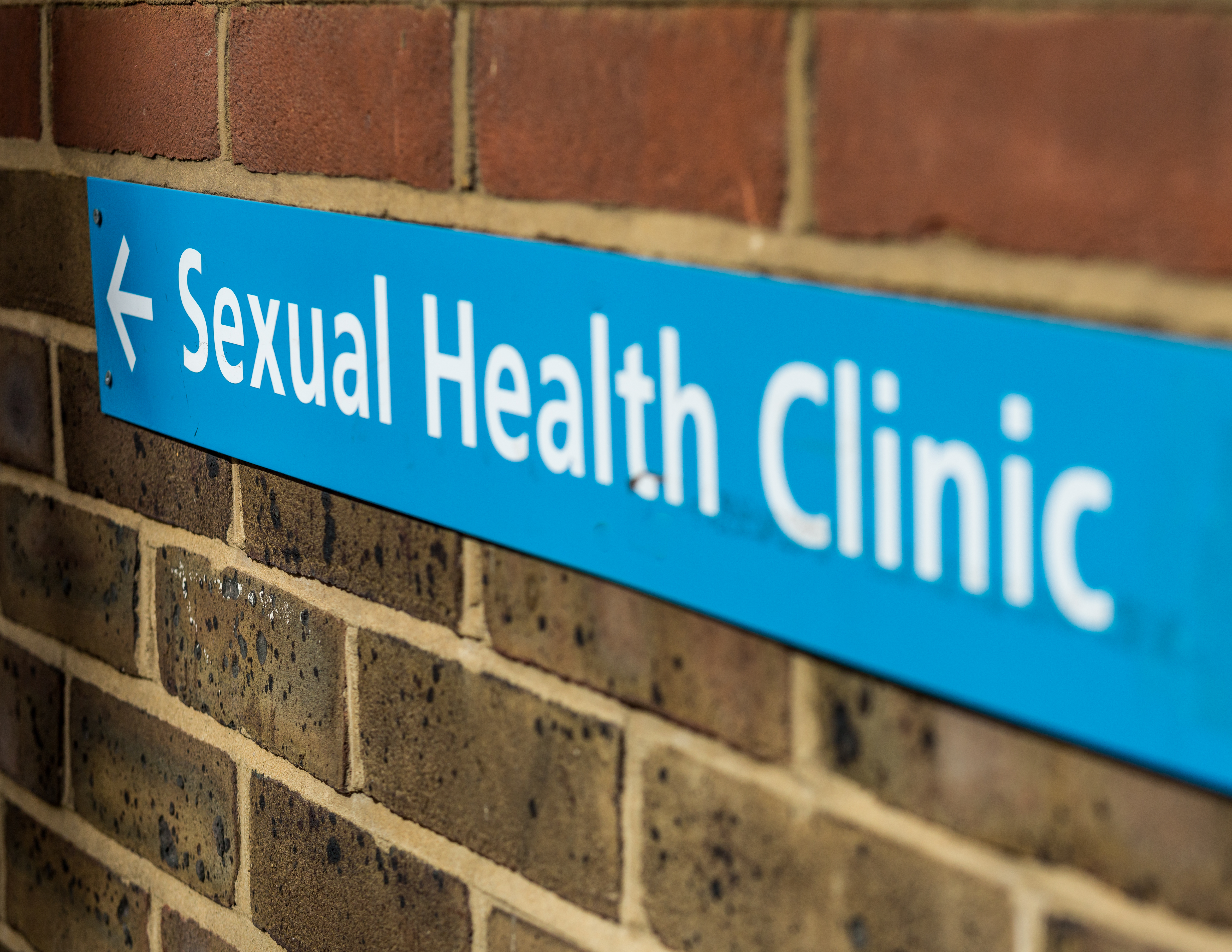 blue sign on a brick wall, saying Sexual Health clinic with an arrow pointing the direction to go